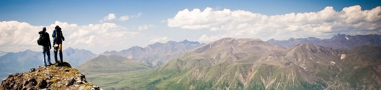 Zwei Bergsteiger überblicken vom Gipfel eines Berges die Umgebung